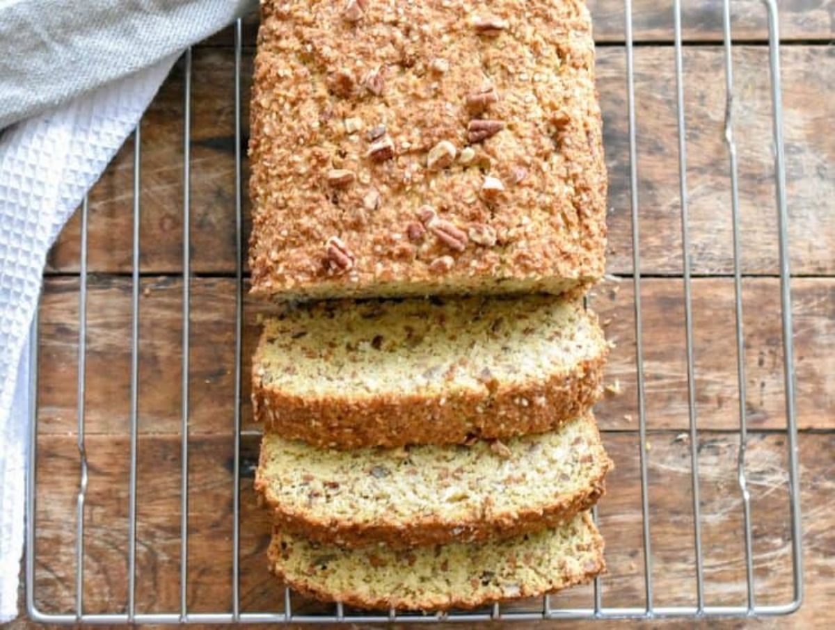 On a wooden table is a wire cooling rack is a rectangular loaf with 3 slices cut from it