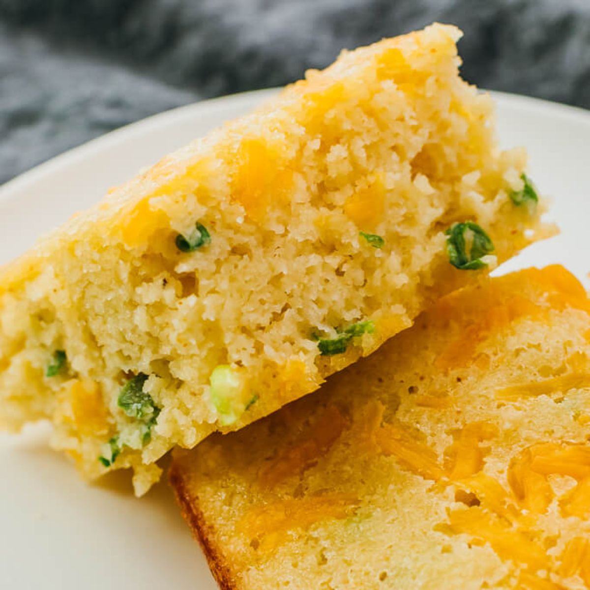 A partial shot of a white plate on a gray background with 2 chunks of herbed bread on it.