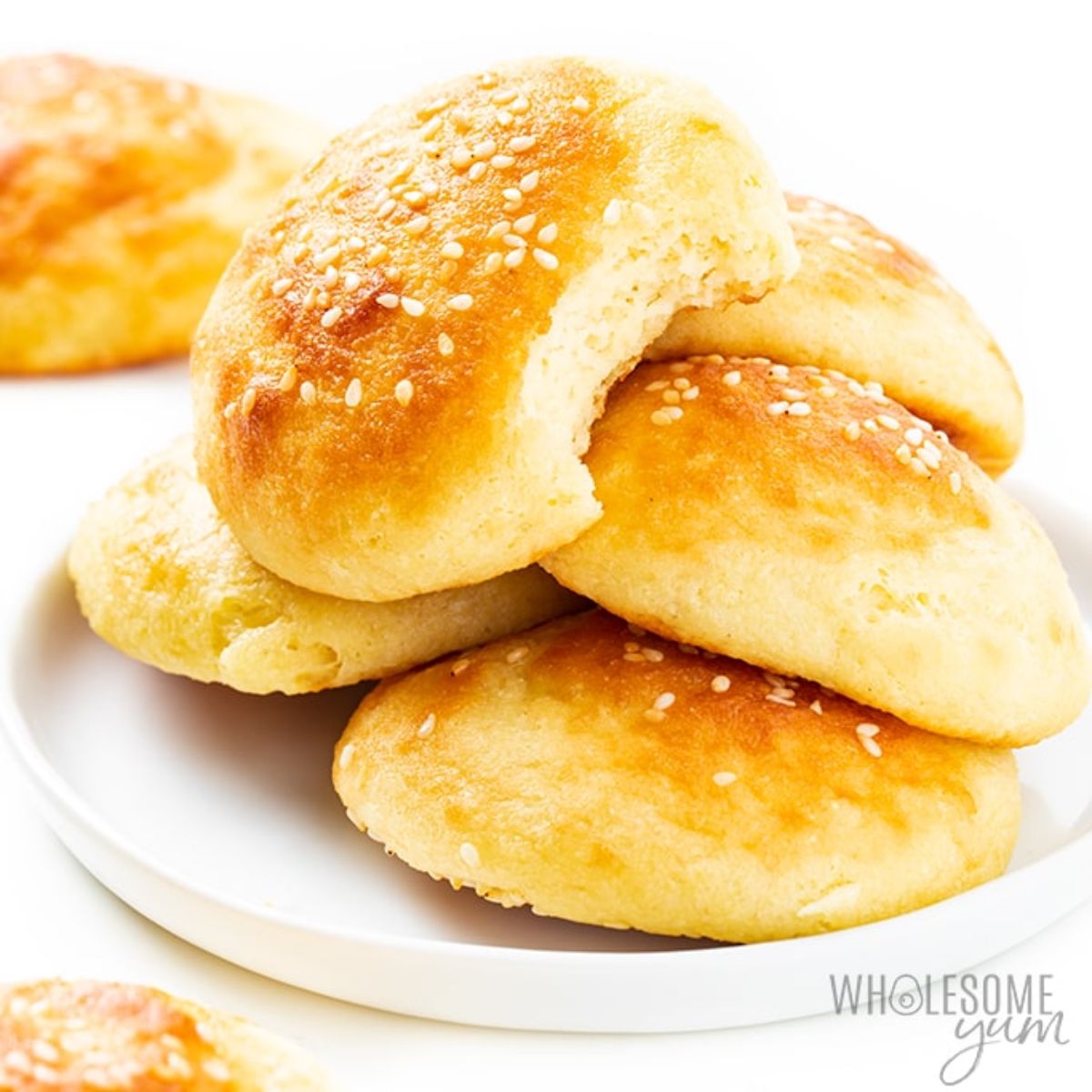 A round white palte with a stack of 5 flat white bread rolls on it. A blurred roll is in the back left of the shot