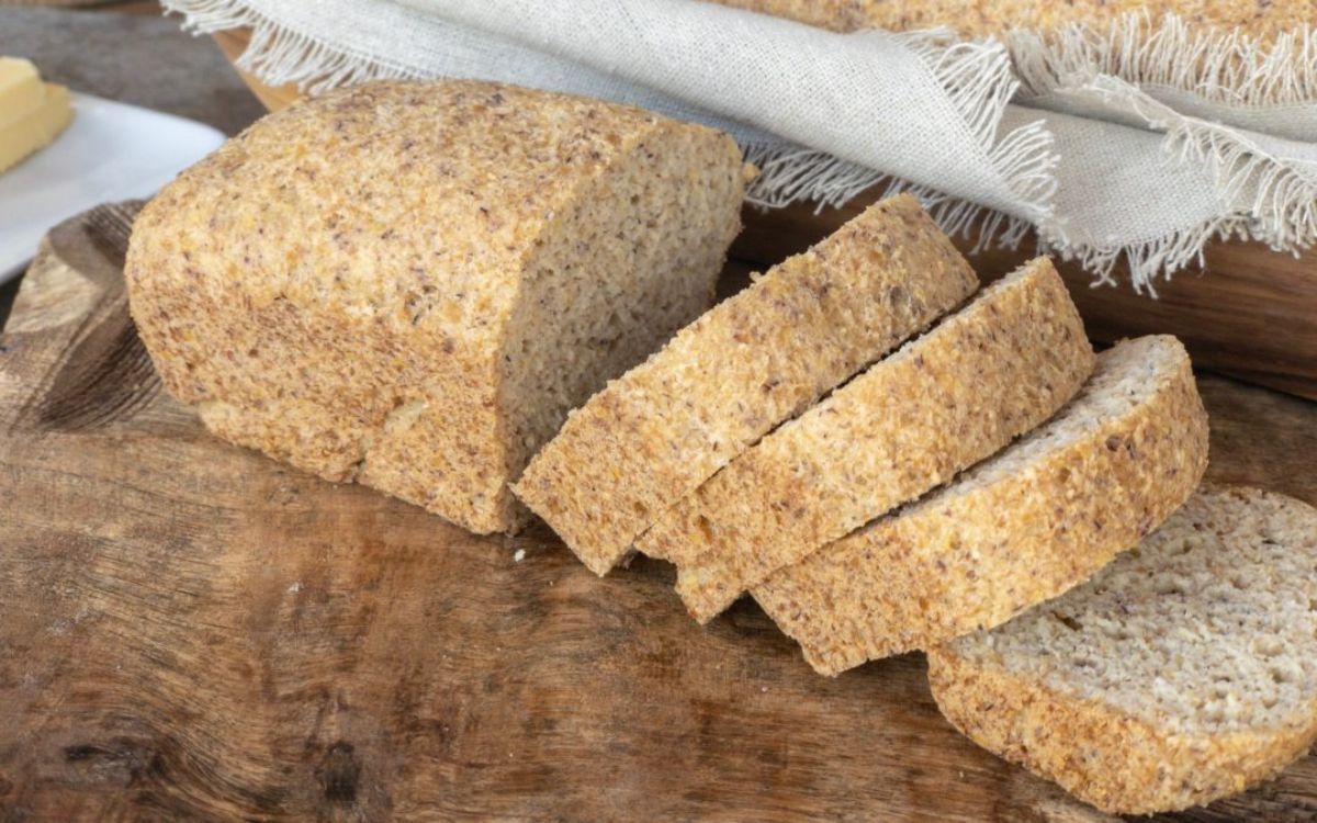 On a wooden board is a loaf of bread with 4 thick slices cut out of it leaing on each other. In the background is a hessian cloth