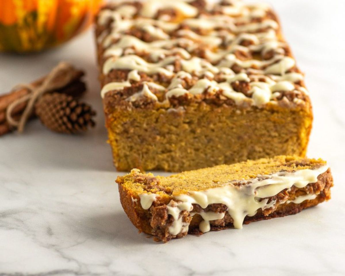 A white surface with a loaf of orange bread. One slice is cut off of the end, and the top is drizzled with icing.